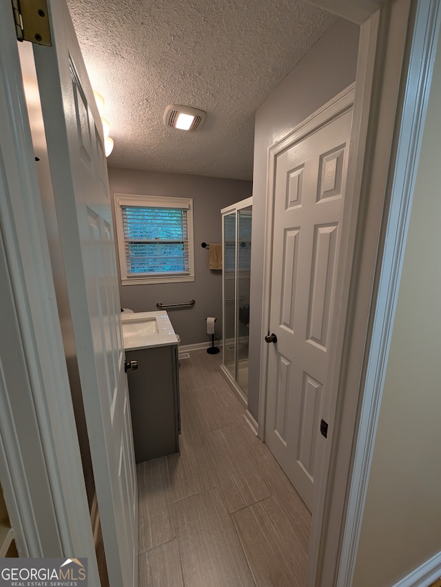 bathroom with vanity, a textured ceiling, and a shower with door