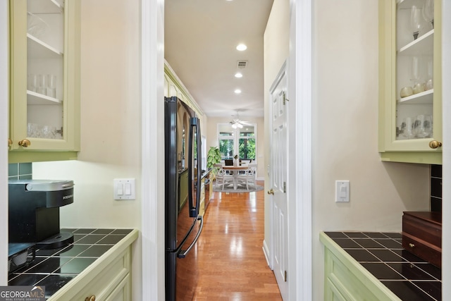 kitchen featuring tile counters, ceiling fan, black fridge, and light wood-type flooring