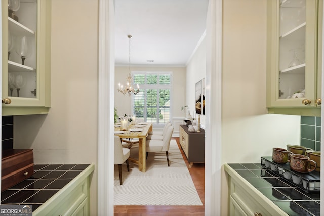 kitchen with pendant lighting, a notable chandelier, hardwood / wood-style floors, tile counters, and crown molding