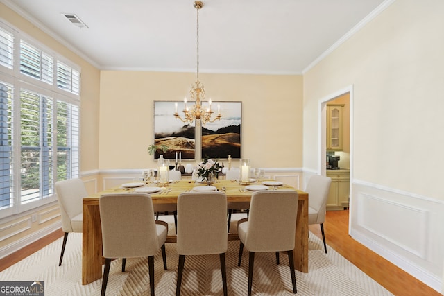 dining room with light wood-type flooring, an inviting chandelier, and ornamental molding