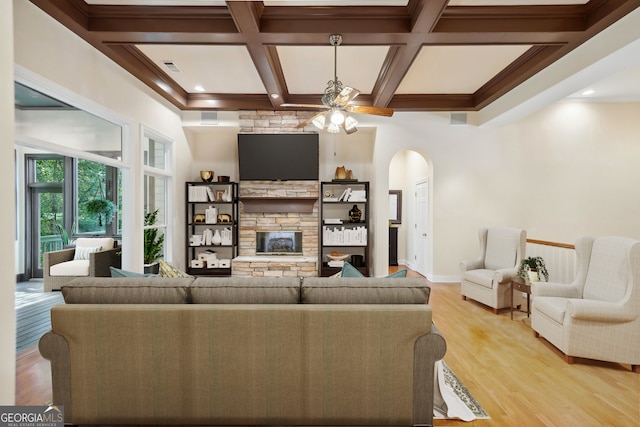 living room with light hardwood / wood-style flooring, coffered ceiling, ceiling fan, and a stone fireplace