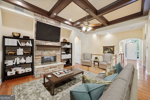 living room with coffered ceiling, a stone fireplace, beam ceiling, hardwood / wood-style flooring, and ceiling fan