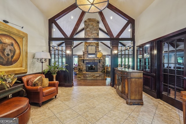 interior space featuring high vaulted ceiling, light hardwood / wood-style flooring, decorative columns, and a stone fireplace