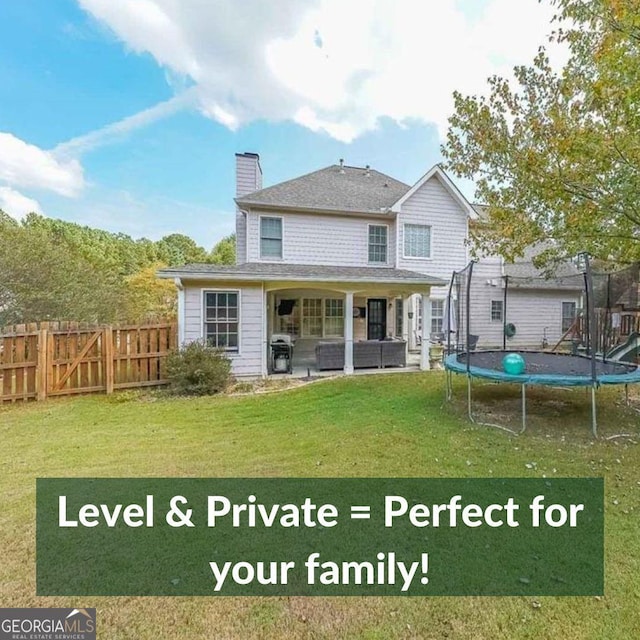 back of property with a fenced backyard, a chimney, a trampoline, a yard, and outdoor lounge area