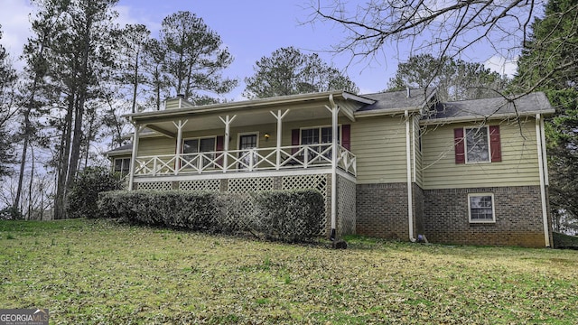 back of property with a porch, brick siding, a yard, and a chimney