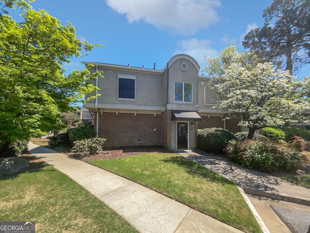traditional home with brick siding, a front yard, and stucco siding