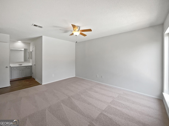 interior space with a sink, a textured ceiling, baseboards, visible vents, and a ceiling fan