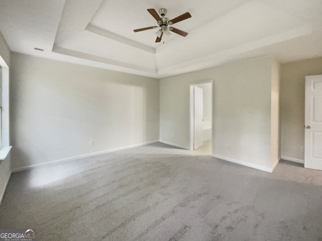 empty room with a tray ceiling, ceiling fan, and carpet