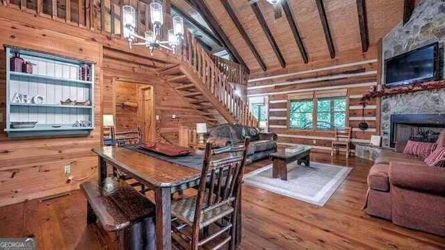 dining room featuring wood-type flooring, a fireplace, beam ceiling, and wooden walls