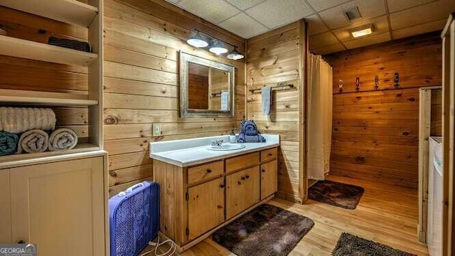 bathroom with wood-type flooring, wooden walls, a drop ceiling, and vanity