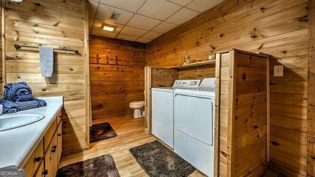 washroom featuring separate washer and dryer, sink, wooden walls, and light hardwood / wood-style floors