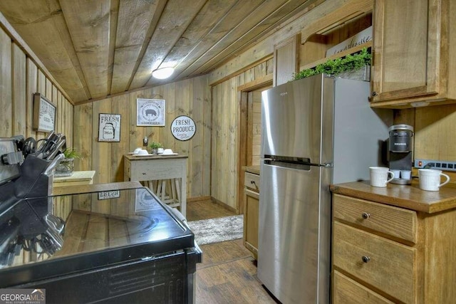 kitchen with vaulted ceiling, hardwood / wood-style floors, wood ceiling, stainless steel refrigerator, and wooden walls