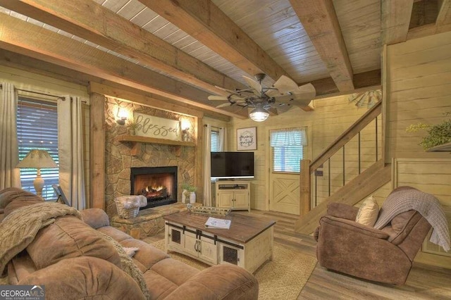 living room featuring a fireplace, light hardwood / wood-style flooring, wood ceiling, ceiling fan, and beam ceiling