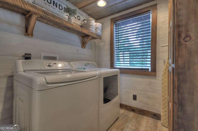 clothes washing area with independent washer and dryer, wood walls, and light hardwood / wood-style floors