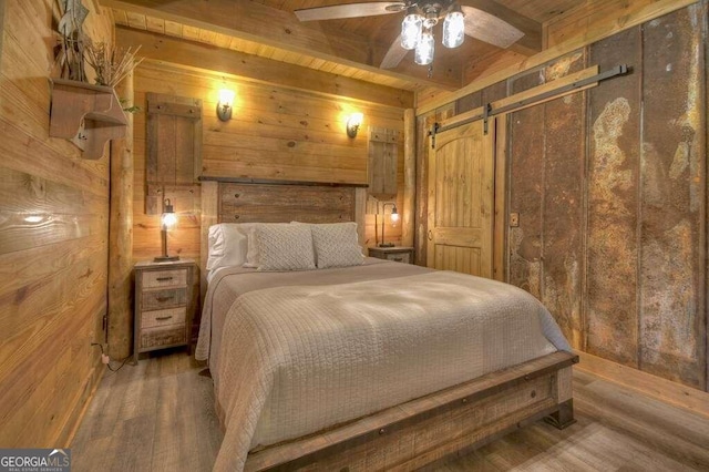 bedroom with wood walls, wooden ceiling, hardwood / wood-style floors, a barn door, and ceiling fan