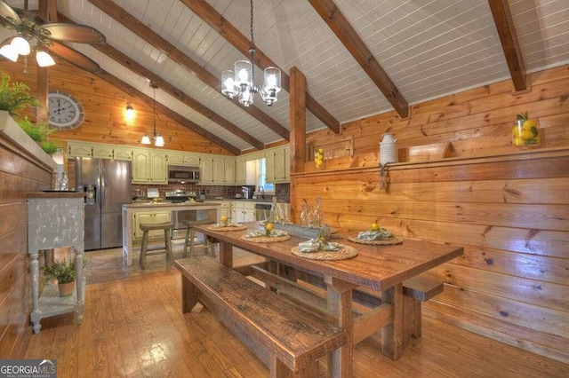 dining space with wooden walls, light wood-type flooring, ceiling fan with notable chandelier, beamed ceiling, and high vaulted ceiling