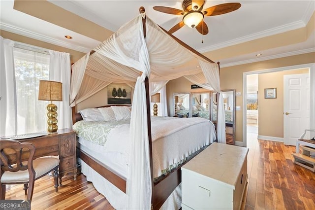 bedroom with crown molding, wood-type flooring, a tray ceiling, and ceiling fan