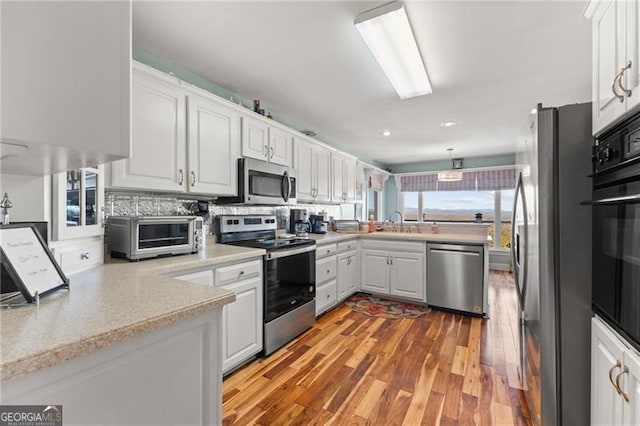 kitchen featuring hardwood / wood-style floors, appliances with stainless steel finishes, white cabinetry, sink, and tasteful backsplash