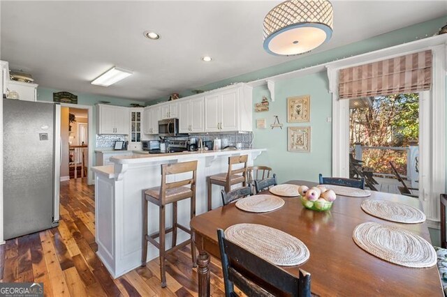 kitchen featuring hardwood / wood-style floors, stainless steel appliances, white cabinetry, kitchen peninsula, and tasteful backsplash