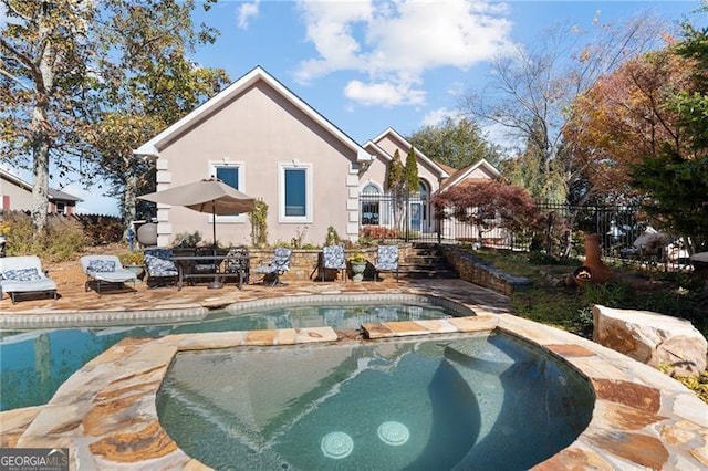 back of property featuring fence, a fenced in pool, an in ground hot tub, stucco siding, and a patio area