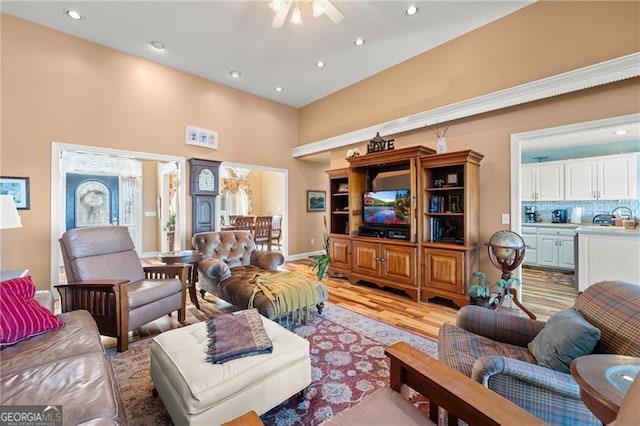 living room with ceiling fan, light hardwood / wood-style floors, and a towering ceiling