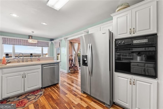 kitchen featuring decorative light fixtures, wood-type flooring, appliances with stainless steel finishes, sink, and white cabinetry