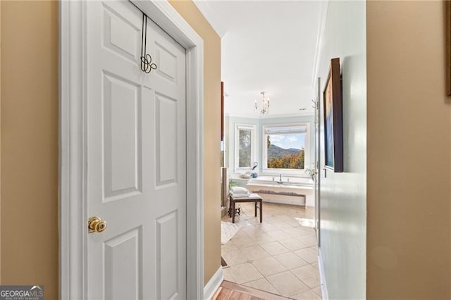 corridor with ornamental molding, a chandelier, and light tile patterned flooring