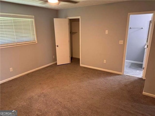 unfurnished bedroom with dark colored carpet, ceiling fan, a walk in closet, and a closet