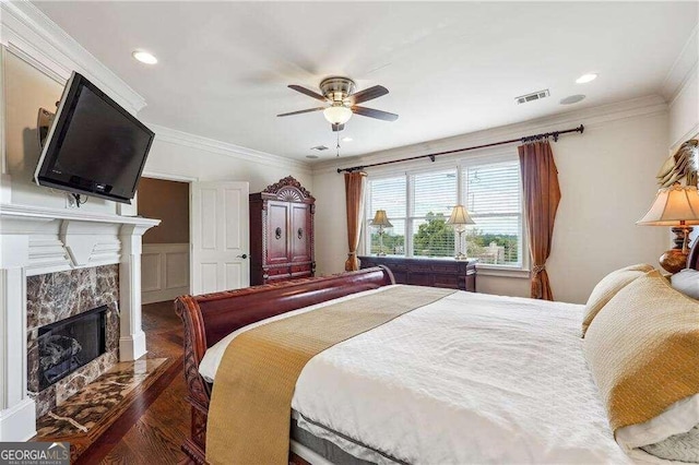 bedroom featuring ceiling fan, a tiled fireplace, dark hardwood / wood-style floors, and crown molding