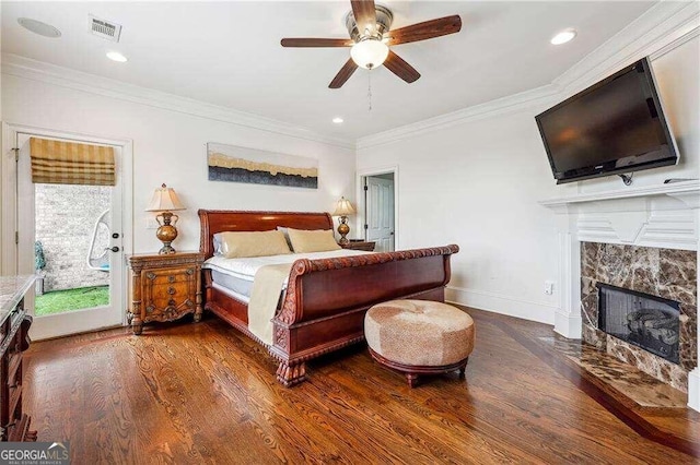 bedroom featuring a tiled fireplace, dark wood-type flooring, ornamental molding, and ceiling fan