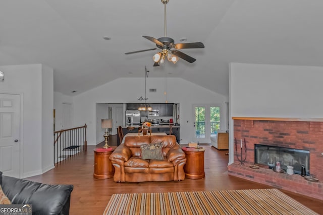 living area with a ceiling fan, lofted ceiling, wood finished floors, and a brick fireplace