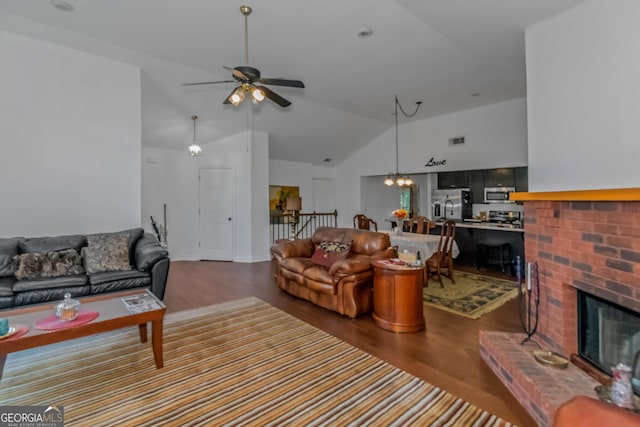 living area with wood finished floors, ceiling fan, vaulted ceiling, a fireplace, and a chandelier