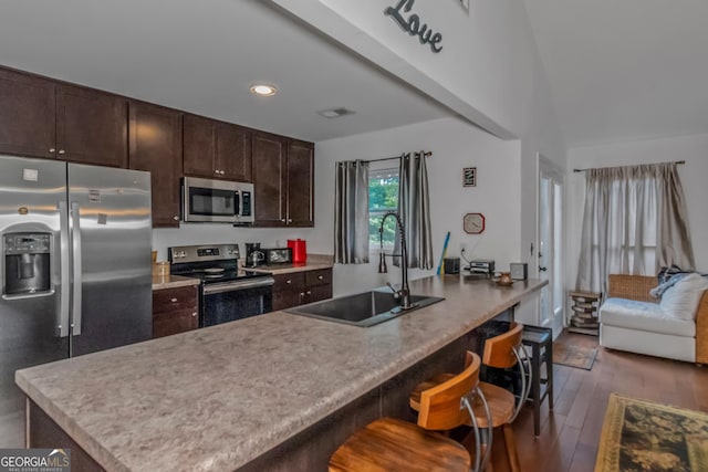 kitchen featuring dark brown cabinets, a kitchen bar, dark wood-type flooring, stainless steel appliances, and sink