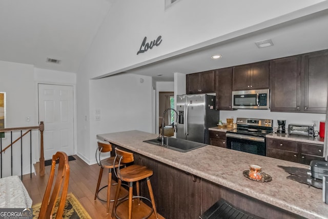 kitchen with stainless steel appliances, a sink, vaulted ceiling, wood finished floors, and a breakfast bar area