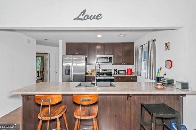 kitchen with stainless steel appliances, dark brown cabinetry, a sink, a kitchen breakfast bar, and light countertops