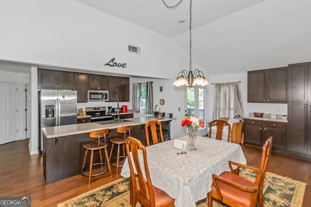 dining space featuring high vaulted ceiling, sink, wood-type flooring, and a chandelier