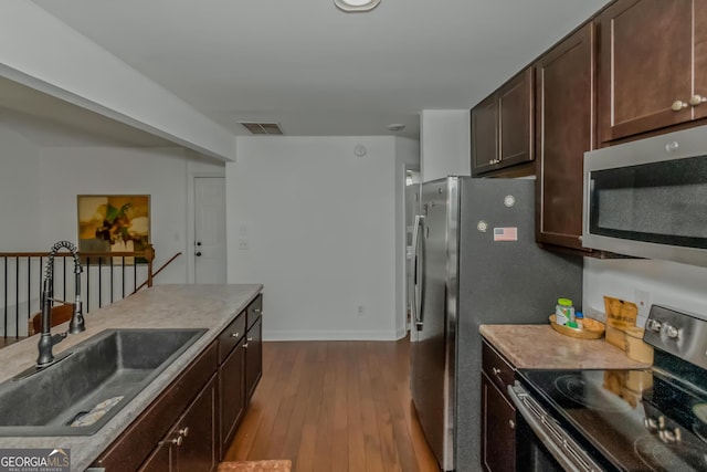 kitchen featuring appliances with stainless steel finishes, a sink, dark wood-style flooring, dark brown cabinetry, and light countertops