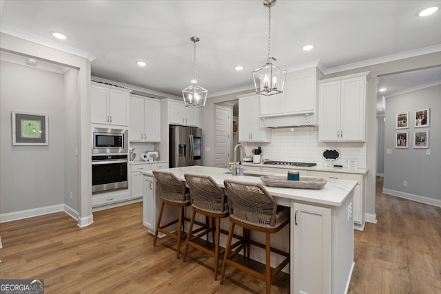 kitchen with a breakfast bar area, light hardwood / wood-style flooring, pendant lighting, appliances with stainless steel finishes, and an island with sink