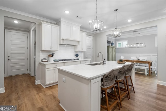 kitchen with stainless steel gas cooktop, a breakfast bar area, a center island with sink, white cabinets, and light hardwood / wood-style floors