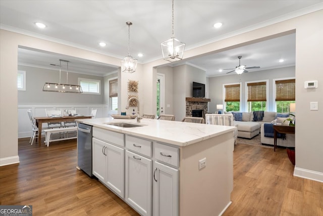 kitchen with ceiling fan with notable chandelier, light hardwood / wood-style floors, an island with sink, a brick fireplace, and white cabinets