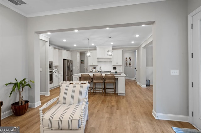 kitchen featuring light wood-type flooring, stainless steel appliances, an island with sink, a kitchen bar, and tasteful backsplash