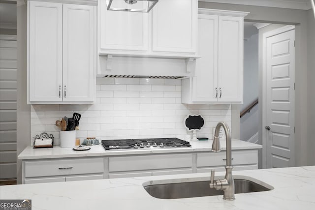 kitchen featuring light stone countertops, stainless steel gas stovetop, backsplash, sink, and white cabinets