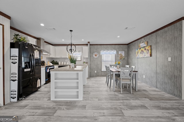 kitchen with a kitchen island, black appliances, pendant lighting, white cabinetry, and wall chimney range hood