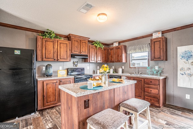 kitchen featuring a textured ceiling, black appliances, a center island, sink, and hardwood / wood-style flooring