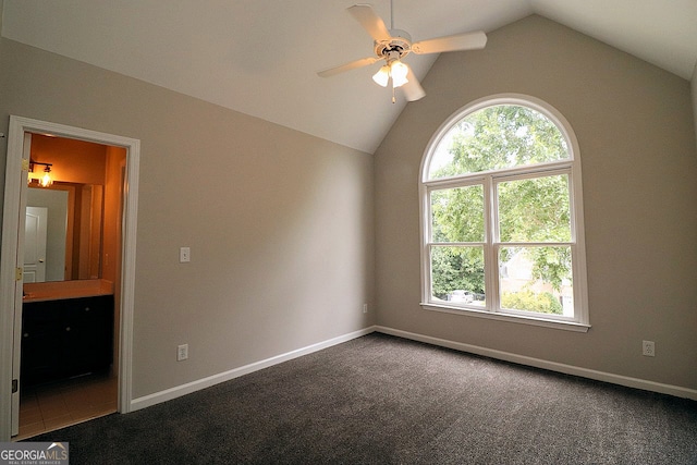 interior space with dark carpet, ceiling fan, ensuite bath, and vaulted ceiling