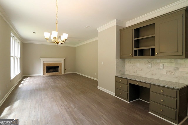 unfurnished living room with built in desk, an inviting chandelier, a fireplace, dark wood-type flooring, and ornamental molding