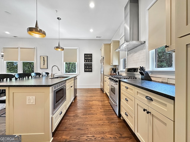 kitchen with wall chimney exhaust hood, appliances with stainless steel finishes, an island with sink, dark wood-type flooring, and sink