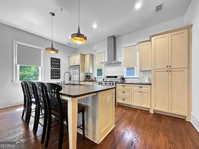 kitchen with a kitchen breakfast bar, dark hardwood / wood-style floors, a center island with sink, hanging light fixtures, and wall chimney range hood