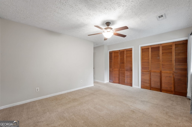 unfurnished bedroom featuring ceiling fan, light colored carpet, a textured ceiling, and two closets