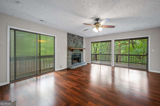 unfurnished living room with a textured ceiling, ceiling fan, hardwood / wood-style flooring, and a stone fireplace